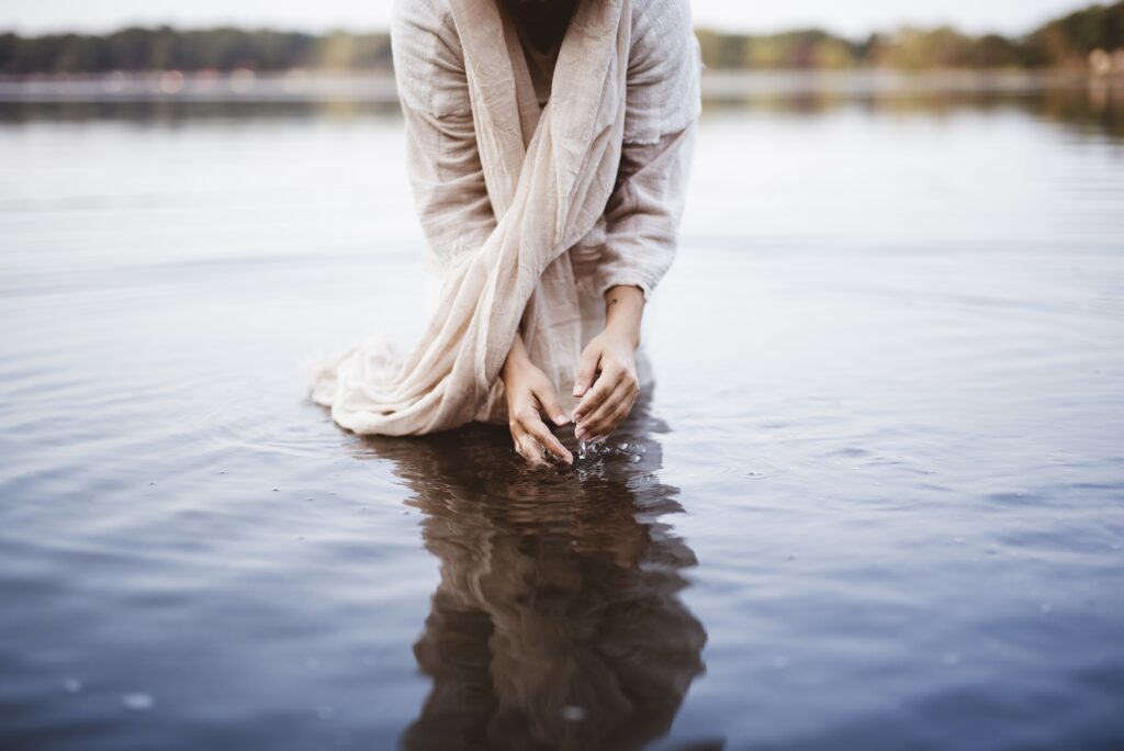 Female wearing a biblical robe while standing in the water and washing her hands