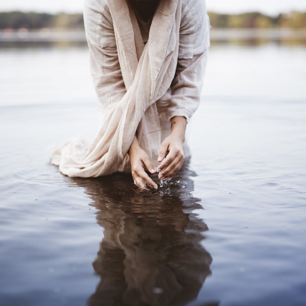 Female wearing a biblical robe while standing in the water and washing her hands