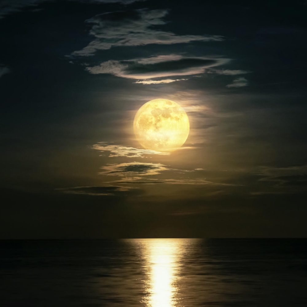 Super full moon and cloud in the yellow sky above the ocean horizon at midnight, moonlight reflect the water surface and wave, Beautiful nature landscape view at night scene of the sea for background